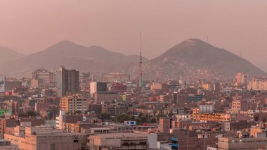 Gün batımında Lima şehrinin panoramik ufuk çizgisi ve birçok binanın havadan zaman çizelgesi. Arka planda tepeler olan fakir evler. Sokakta trafik vardı. Lima, Peru