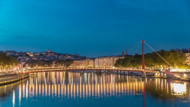 Lyon 'daki Saone Nehri' nin üzerindeki Palais du Justice Köprüsü 'nde, günden geceye geçiş. Rıhtımdaki aydınlık binalar gün batımından sonra suya yansıyor.