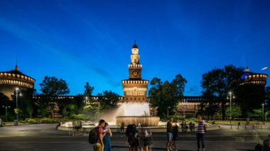 Sforza Kalesi 'nin ana girişi, ön manzara ve kule Castello Sforzesco, geçiş zamanı olan Milan, İtalya' yı aydınlattı. Çeşme ve etrafta dolaşan insanlar.