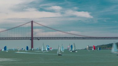 25 Nisan sualtı köprüsü ile Tagus nehrinde yelkenli balıklar arka planda Almada ve Lizbon 'u Portekiz zaman diliminde bulutlu mavi gökyüzü ve birçok tekneye bağlıyor.