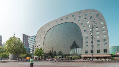 Rotterdamse Markthal 'ın dış yüzeyinde aşırı kayma. Dükkanları ve restoranları olan ikonik at nalı şeklinde bir bina. Meydanda gezinen insanlar. Gökdelenler ve arka planda canlı bir şehir manzarası