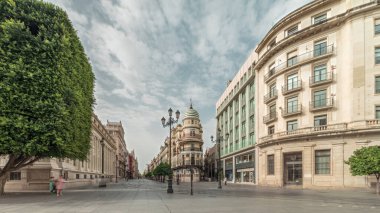 Avda boyunca yürüyen yayalar. De la Constitucion, Seville, İspanya 'nın Casco Antiguo bölgesindeki ana cadde. Edificio de la Adriatica ile zaman atlaması, tarihi binalar ve geçen tramvaylar