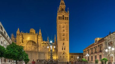 La Giralda ve Seville Katedrali günden geceye geçiş zamanı, gün batımından sonra altın ışıklarla parıldıyor. Tarihi çan kulesi, gotik detaylar ve Seville, İspanya 'da aydınlatılmış sokaklar.