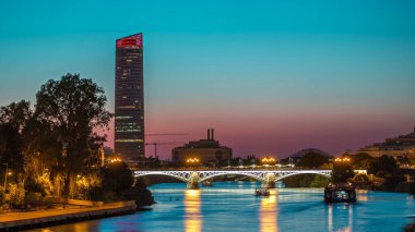 Guadalquivir Nehri yakınlarındaki Torre Sevilla gökdeleninin yer aldığı Seville 'in ufuk çizgisi gece gündüz geçiş zamanı. Aydınlatılmış Triana Köprüsü su, modern ve geleneksel mimariyi yansıtıyor