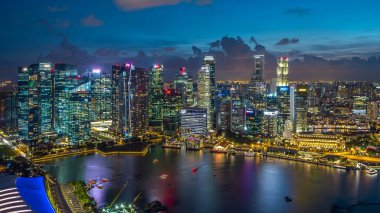 Aerial view of Singapore business district skyscrapers at evening with water reflections day to night timelapse. Panorama of illuminated towers with blinking lights in windows