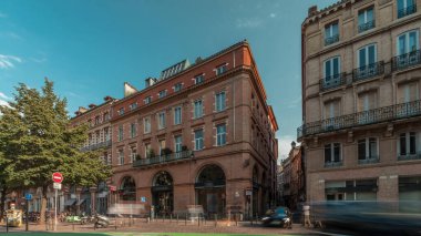Toulouse, Occitanie, Fransa 'da Rue de Metz' in zaman çizelgesini gösteren panorama, tarihi cepheleri, dükkanları, kafeleri, trafiği ve mavi bulutlu gökyüzünü gösteriyor. Şehrin göbeğinde canlı bir şehir manzarası