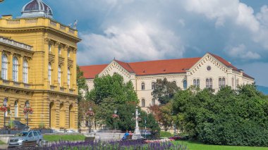 The building of the Croatian National Theater timelapse. Croatia, Zagreb. Green lawn with flowerbed and blue cloudy sky
