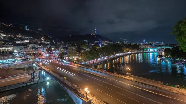 Gürcistan 'ın Tiflis şehrinde ahşap oyulmuş balkonlu renkli geleneksel evleri gösteren panorama. Aydınlatılmış binalar ve nehir üzerindeki bir köprüde trafik