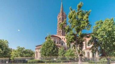 Fransa 'nın Toulouse kentindeki Saint Sernin Bazilikası' nın kaldırımlı parvisleri. Zaman atlaması. Avrupa 'nın en büyük Roma kilisesi tuğla çan kulesi, kemerli kapılar, yeşil ağaçlar ve mavi gökyüzü.