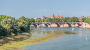 Toulouse, Fransa 'da Garonne River ve Pont Neuf saatleri. Rönesans kemer köprüsü mavi gökyüzünün altındaki suya Daurade Leydisi Bazilikası ile yansıyor. Yeşil ağaçlı rıhtım