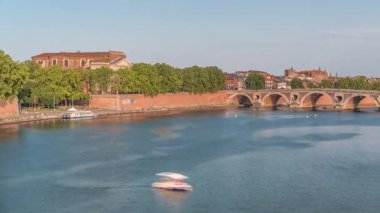 Toulouse, Fransa 'da Port de la Daurade ile Garonne Nehri ve Pont Neuf zamanapse. Bu Rönesans kemer köprüsü bulutlu mavi gökyüzünün altındaki suya yansıyor. Yeşil ağaçlı rıhtım