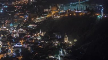 Georgia 'nın Tiflis şehrinde ahşap oymalı balkonları olan renkli geleneksel evler. Aydınlatılmış binalar, teleferik ve yol trafiği