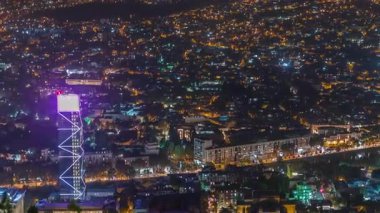 Gürcistan 'ın gökdelenleri, işlek bulvarda yer alan Tiflis hava zaman çizelgesinde aydınlatılmış cam kule. Tarihi bina ve nehir. Bakış açısından bak