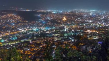 Tiflis şehir manzarası, Gürcistan günden geceye zaman. Şehir merkezinin ve Tiflis 'teki Kura Nehri' nin üst manzarası. Gökyüzünden Gürcistan başkentinin gökyüzü manzarası aydınlatılmış ünlü simgelerle