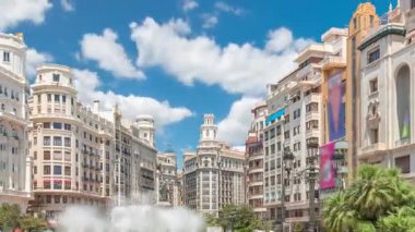 Valencia, İspanya 'da Belediye Meydanı Plaza del Ayuntamiento zaman atlaması hipervane. Büyük mimari, çiçek açan yeşillik ve bulutlu bir gökyüzünün altında su jetleri. İnsanlar canlı meydanda geziniyor..