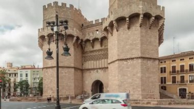 Serrans Kuleleri Torres de Serranos zaman atlaması. Valencia, İspanya 'da. Şehrin antik duvarlarından gelen büyük bir ortaçağ kapısı. Bulutlu bir gökyüzü altında hareketli bir sokak manzarası bu tarihi yeri çerçeveler.