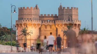 Serrans Kuleleri Torres de Serranos günden geceye Valencia, İspanya 'daki geçiş zamanı. Şehrin antik duvarlarından gelen büyük bir ortaçağ kapısı. İnsanlar tarihi bir dönüm noktasının yakınındaki bir köprüde yürüyorlar.