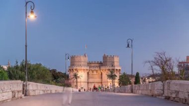 Serrans Kuleleri Torres de Serranos günden geceye Valencia, İspanya 'daki geçiş zamanı. Şehrin antik duvarlarından gelen büyük bir ortaçağ kapısı. İnsanlar tarihi bir yere yakın bir köprüde yürüyorlar.