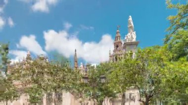 Plaza del Triunfo zaman atlaması ve Sevilla Katedrali 'nin kusursuz gebelik anıtı. Yeşil ağaçlar, tarihi mimari, bulutlu mavi gökyüzü. Endülüs, İspanya 'da manzara