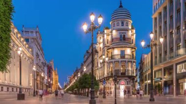 Avenida de la Constitucion, Seville, İspanya 'da günden geceye zaman dilimi. Iconic Adriatica binası gün batımından sonra parlıyor. Modern sokak lambaları, yayalar ve şehir atmosferine sahip tarihi mimari