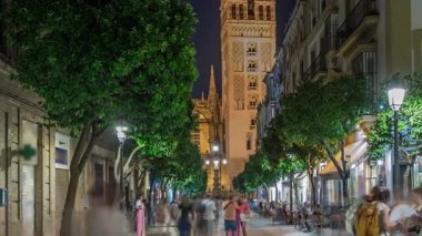 Barrio Santa Cruz 'un Seville, İspanya' daki gece zamanı. Arka planda Giralda kulesi aydınlanıyor. Turistler ve yerliler kafeler ve dükkanlarla dolu büyüleyici kaldırım taşları caddelerinde yürüyorlar..