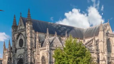 Bordeaux, Fransa 'daki Basilique Saint-Michel zaman çizelgesi, yüksek kulesi olan gotik bir simgedir. İnsanlar yakındaki kafeleri seviyor, yeşil ağaçların altında ve mavi bulutlu gökyüzü, şehrin canlı cazibesini yakalıyor.