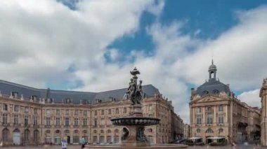 Place de la Bourse zaman atlaması Fransa 'nın Bordeaux şehrinde, Bulutlu mavi gökyüzünün altında klasik mimari ile çevrili Üç Zarafet Çeşmesi ile birlikte. Meydanda yürüyen insanlar.