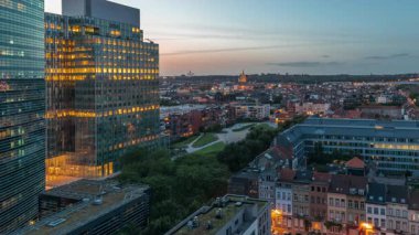 Brüksel kentsel manzarasının yerleşim alanlarıyla ofis gökdelenlerini harmanlayan hava gününden geceye geçiş zamanı. Yeşil park çimenleri, tarihi çatılar ve Belçika 'nın modern mimarisi.