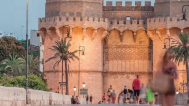 Serrans Kuleleri Torres de Serranos günden geceye Valencia, İspanya 'daki geçiş zamanı. Şehrin antik duvarlarından gelen büyük bir ortaçağ kapısı. İnsanlar tarihi bir dönüm noktasının yakınındaki bir köprüde yürüyorlar.