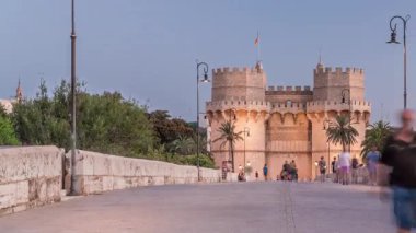 Serrans Kuleleri Torres de Serranos günden geceye Valencia, İspanya 'daki geçiş zamanı. Şehrin antik duvarlarından gelen büyük bir ortaçağ kapısı. İnsanlar tarihi bir yere yakın bir köprüde yürüyorlar.