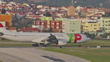 Lizbon Humberto Delgado Havaalanı 'nda arka planda tepeler ve şehir manzarası olan bir uçak hareket ediyor. Portekiz 'de güneşli bir günde havalanmadan önce uçak taksisi. Yandan görüntüle