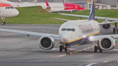 Yoğun bir Lizbon havaalanının pistinde ticari uçaklar Ryanair taksileri, terminaller, diğer uçaklar ve arka planda bir şehir manzarası. Hava taşımacılığının ve havacılığın canlı atmosferi