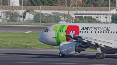 Lizbon Havaalanı 'na indikten sonra terminallere giden ticari bir uçak. TAP Air Portugal Havayolları, güneşli bir günde arka planda şehir silueti ve havaalanı altyapısı olan taksiler üzerinde hareket ediyor.