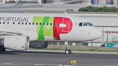 Lizbon Havaalanı 'na indikten sonra terminallere giden ticari bir uçak. TAP Air Portugal Havayolları, güneşli bir günde arka planda şehir silueti ve havaalanı altyapısı olan taksiler üzerinde hareket ediyor.