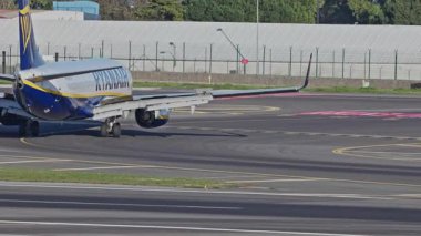 Lizbon Havaalanı 'na indikten sonra terminallere giden ticari bir uçak. Ryanair Havayolları, güneşli bir günde arka planda şehir silueti ve havaalanı altyapısı olan taksiler üzerinde hareket ediyor.