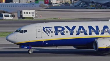 Lizbon Havaalanı 'na indikten sonra terminallere giden ticari bir uçak. Ryanair Havayolları, güneşli bir günde arka planda şehir silueti ve havaalanı altyapısı olan taksiler üzerinde hareket ediyor.