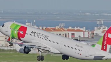 Lizbon Havaalanı 'ndan kalkan uçak. TAP Air Portugal uçaklarının yakın çekim görüntüleri açık mavi gökyüzünün altında şehrin ufuk çizgisi ve havaalanı altyapısı ile kalkıyor.