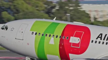 Lizbon Havaalanı 'ndan kalkan uçak. TAP Air Portugal uçaklarının yakın çekim görüntüleri açık mavi gökyüzünün altında şehrin ufuk çizgisi ve havaalanı altyapısı ile kalkıyor.