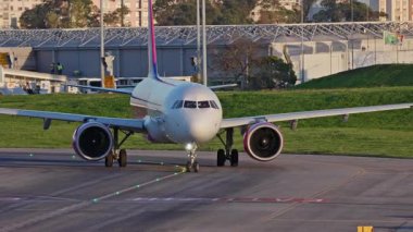 Lizbon 'da yoğun bir havaalanının pistinde ticari uçaklar Wizzair taksileri, terminaller, diğer uçaklar ve arka planda bir şehir manzarası. Hava taşımacılığının ve havacılığın canlı atmosferi