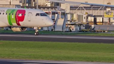 Lizbon 'da yoğun bir havaalanının pistinde yolcu uçakları TAP Air Portugal taksiler, terminaller, diğer uçaklar ve arka planda bir şehir manzarası. Hava taşımacılığının ve havacılığın canlı atmosferi