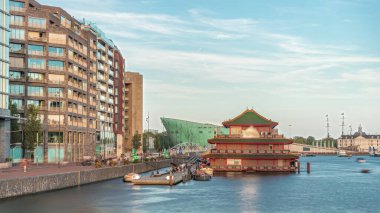 Sudaki pagoda şeklinde bir Çin restoranının hipervanesi, tarihi şehir merkezi binalarının ve günbatımında modern mimarinin arka planına karşı kurulur. Amsterdam, Hollanda
