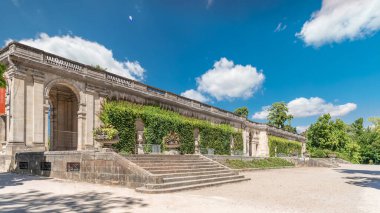 Fransa 'nın başkenti Jardin' de Palais du Capitole 'de zaman atlaması. Sarmaşık kaplı yeşil ağaçlar, merdivenler ve parlak mavi bulutlu gökyüzü ile çevrili tarihi bir binanın manzarası.