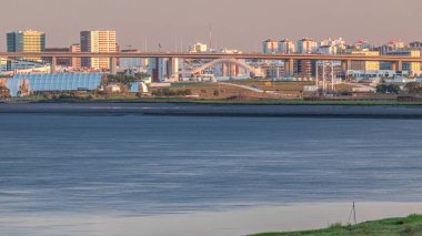 Lizbon 'daki Park Tejo ve River Timelapse' ın arka planında Milletler Bölgesi Modern Mimari Parkı var. Percurso Ribeirinho de Loures 'ten Vasco da Gama Köprüsü