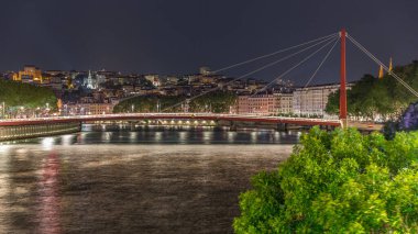 Saone Nehri üzerindeki kırmızı asma köprü ile Lyon 'un şehir manzarasının gece zaman çizelgesi, gece boyunca aydınlatılmış deniz kenarı suya yansıdı. Fransa