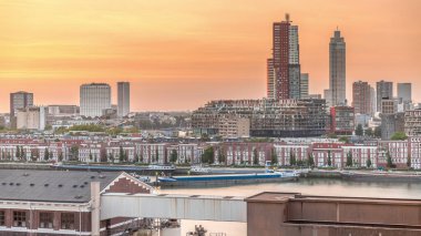 Günbatımında Rotterdam şehir merkezindeki modern binaların hava zaman çizelgesi, Hollanda. Finans bölgesinde kuleler ve gökdelenler, turuncu gökyüzü ile eski fabrika canlı bir ufuk çizgisi oluşturur