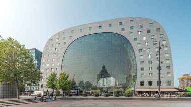 Rotterdamse Markthal 'ın dış yüzeyinde aşırı kayma. Dükkanları ve restoranları olan ikonik at nalı şeklinde bir bina. Meydanda gezinen insanlar. Gökdelenler ve arka planda canlı bir şehir manzarası