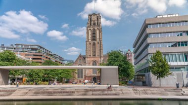 Laurenskerk 'in (Saint Lawrence Kilisesi) Grotekerkplein, Rotterdam' daki hiperlapesi. İnsanlar mavi bulutlu gökyüzünün altında çimlerde dinleniyorlar. Kanal merdivenlerinin yanında saati olan tarihi çan kulesi. Hollanda
