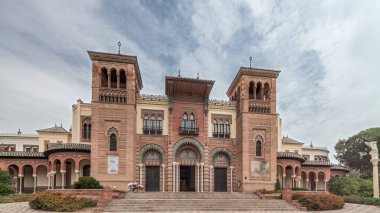 Maria Luisa Park 'taki Sevilla Sanat ve Gelenekler Müzesi cephesi. Plaza de America 'da Mudejar tarzı bir bina var. Bulutlu gökyüzü altında zaman atlaması. Sevilla, İspanya.