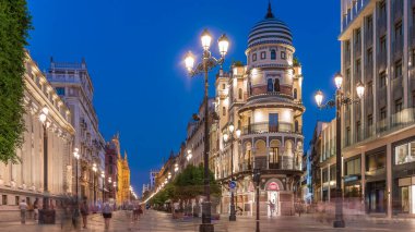 Avenida de la Constitucion, Seville, İspanya 'da günden geceye zaman dilimi. Iconic Adriatica binası gün batımından sonra parlıyor. Modern sokak lambaları, yayalar ve şehir atmosferine sahip tarihi mimari