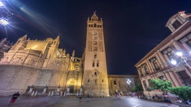 La Giralda ve Seville Katedrali geceleri aşırı hızlanarak altın ışıklarla parıldıyor. Tarihi çan kulesi, gotik detaylar ve aydınlatılmış sokaklar Sevilla, İspanya 'da büyülü bir atmosfer yaratıyor.